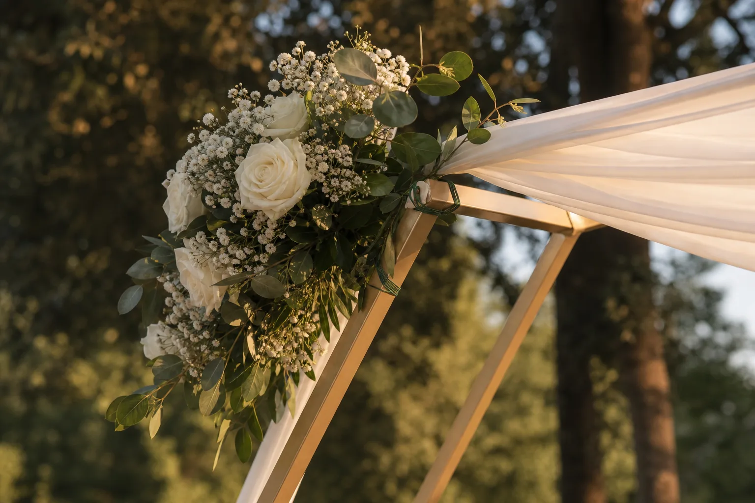White flowers attached to the corner of a gold wedding arch