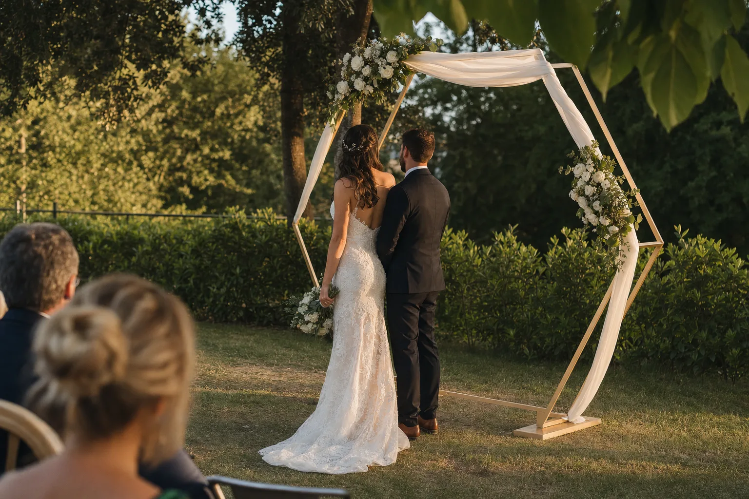 Couple standing beneath a champagne-gold hexagonal wedding arch at a garden ceremony