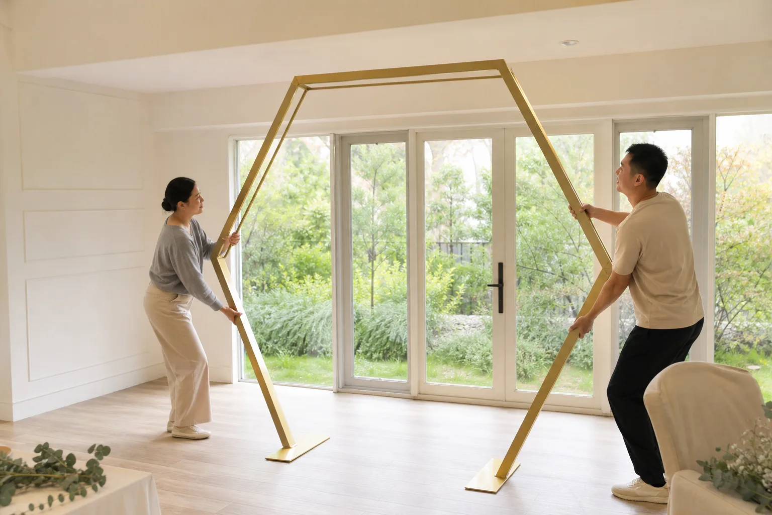 Two adults carefully raising a complete champagne-gold hexagonal wedding arch